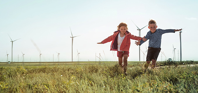 Two children playing in a field with wind turbines behind them